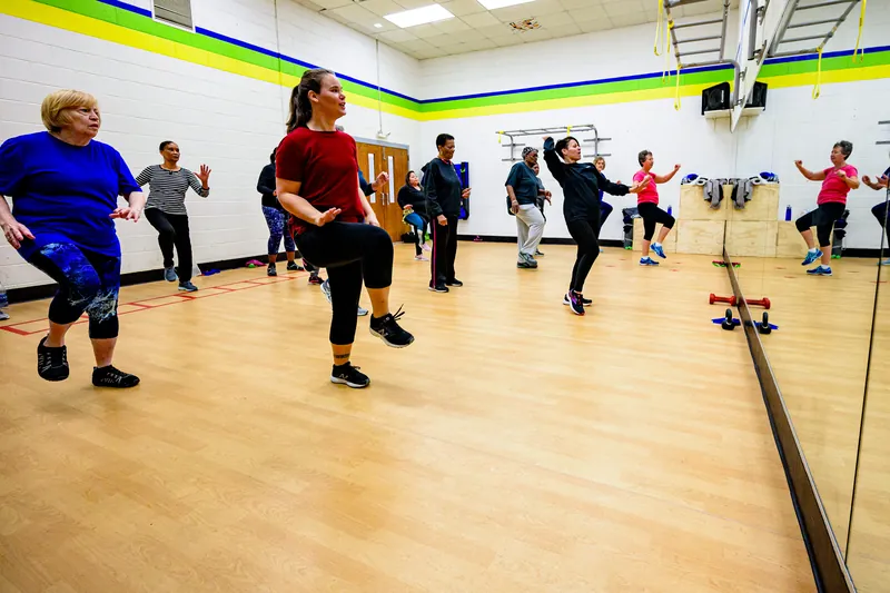 Cours de groupe dans un studio avec miroir : des participantes de tous âges lèvent le genou en rythme.