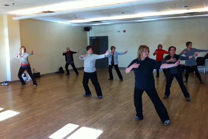 Groupe de participantes en posture de qi gong dans une grande salle au plancher de bois.