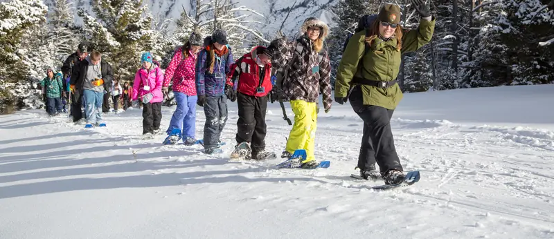 Groupe qui avance en file, raquettes aux pieds, sur la neige ensoleillée, derrière une animatrice souriante.